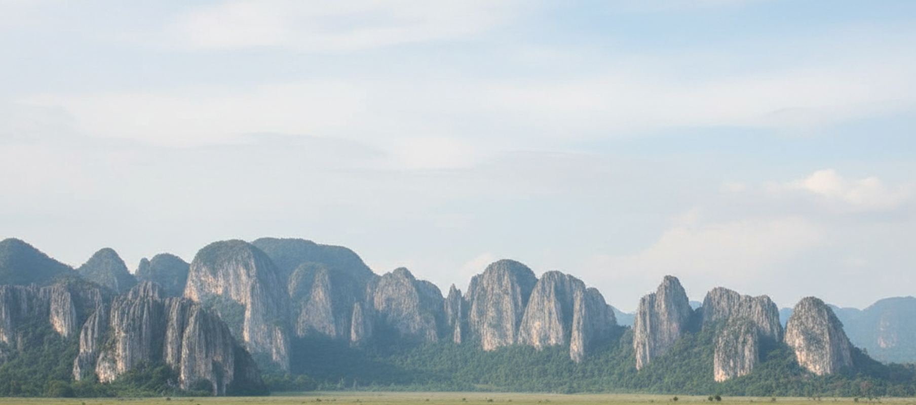 Wide view across flat green ground in the Kinta Valley toward a line of steep gray limestone towers.